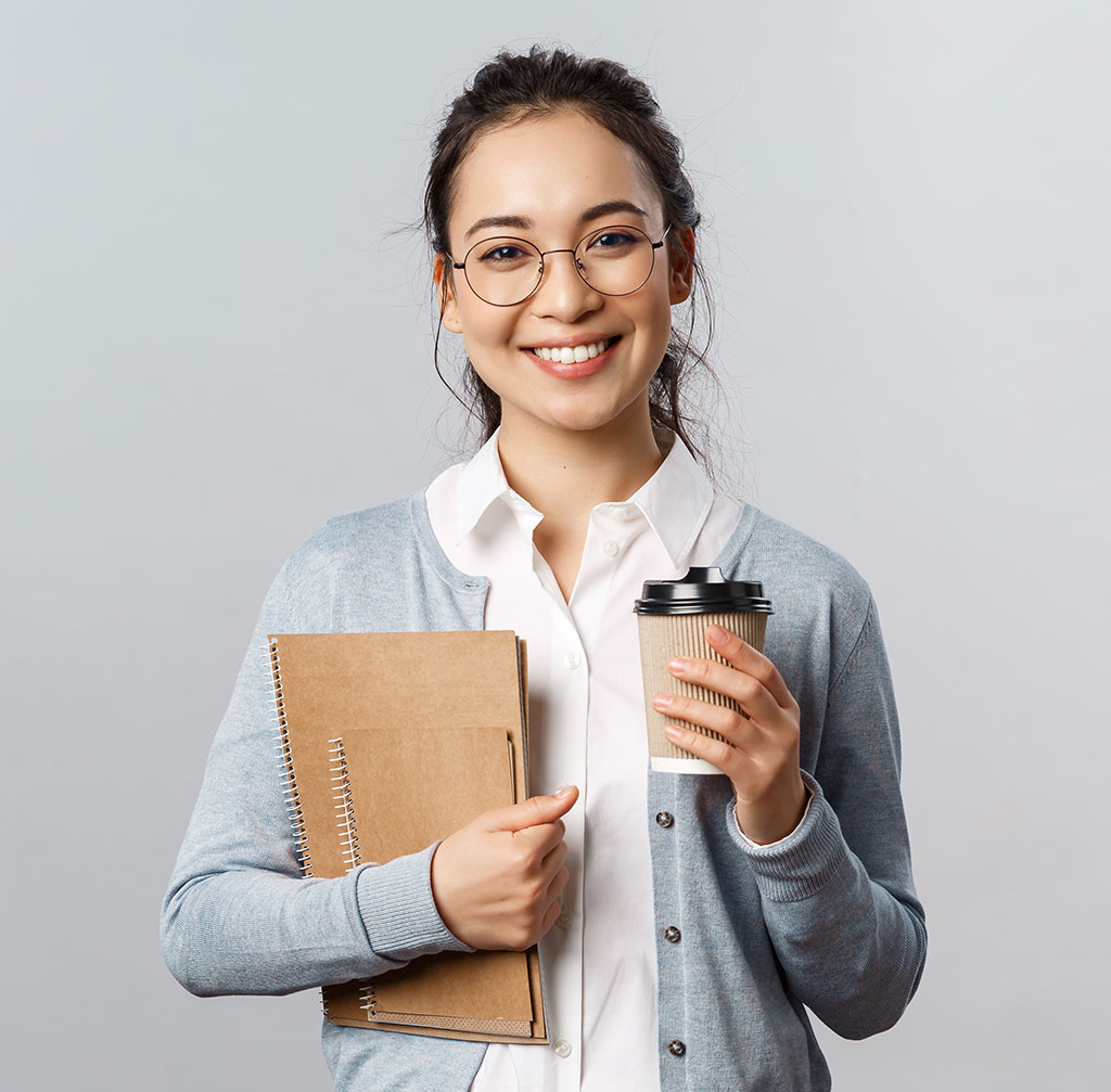 A young adult holding her notebooks and a cup of coffee