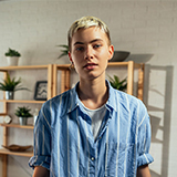 A person with short blonde hair wearing a blue shirt.